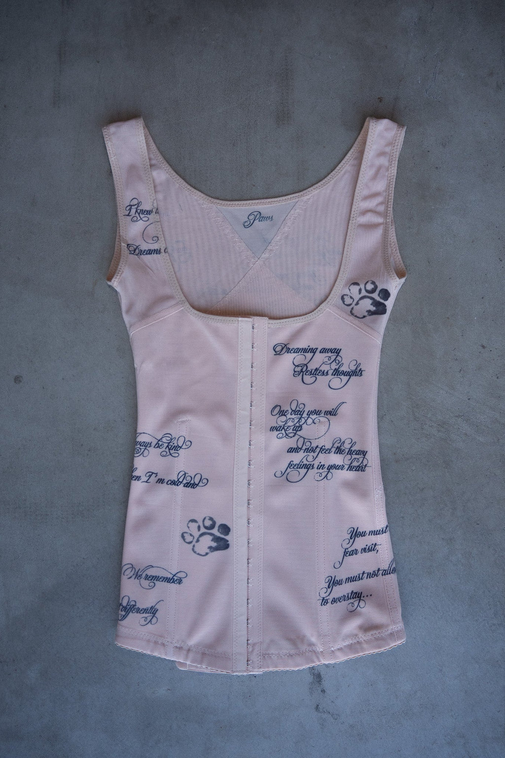 Light nude corset with text and paw prints on a gray surface