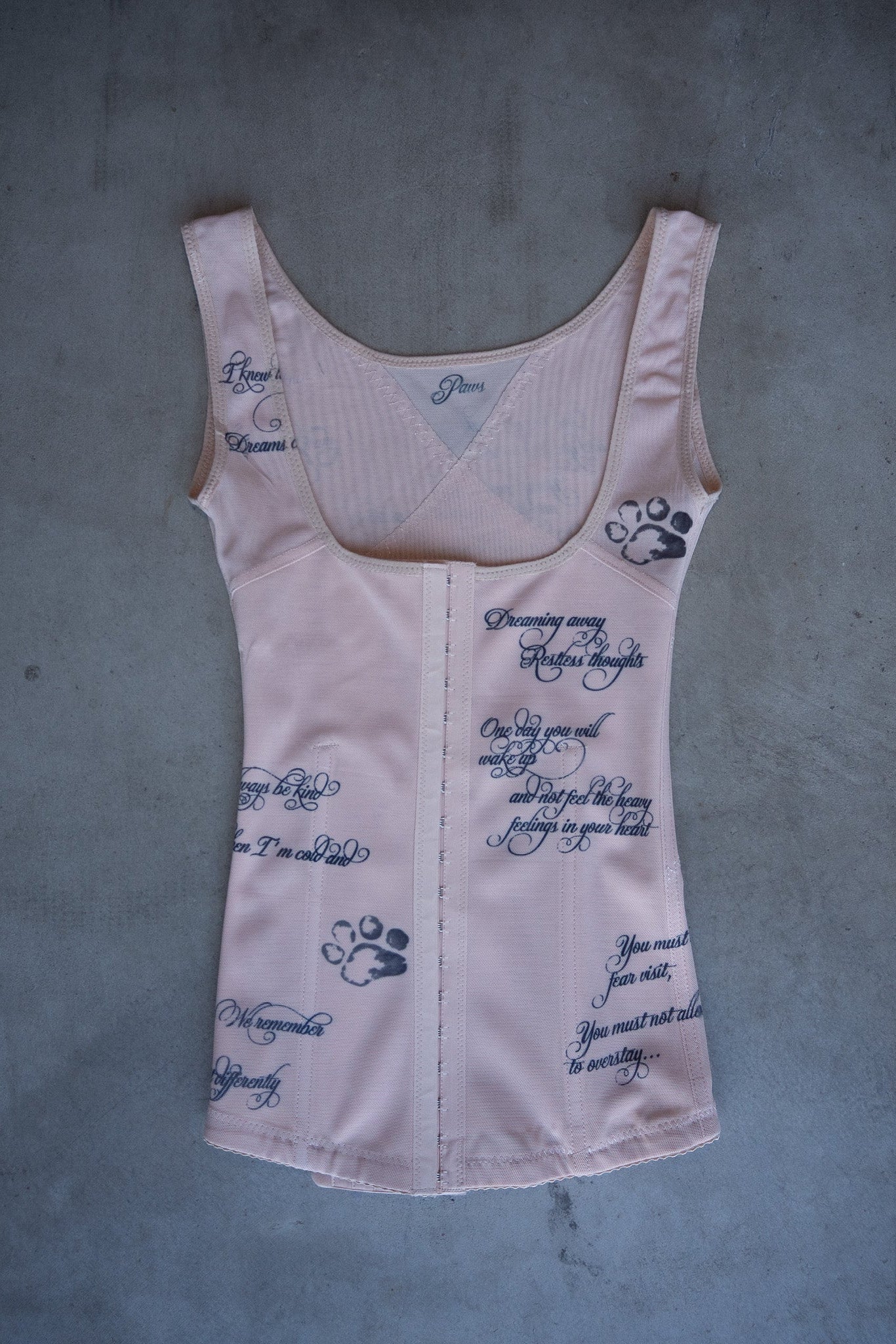 Light nude corset with text and paw prints on a gray surface